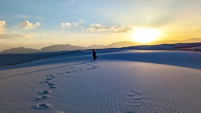 A woman leaves footprints behind on a sand dune at sunset in New Mexico