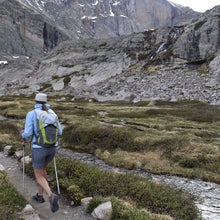 Hiker on a trail through alpine tundra along a stream with the Diamond wall of Longs Peak in the background